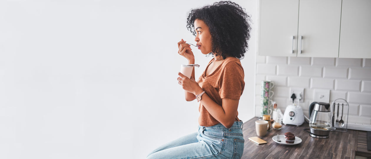 Young woman sitting on the kitchen bench eating yoghurt