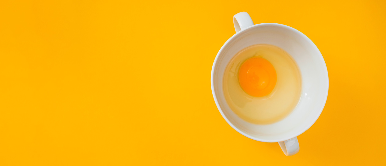 Raw egg in a white mug on a yellow background