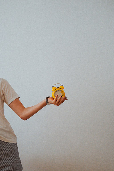 Young woman holding out a yellow alarm clock