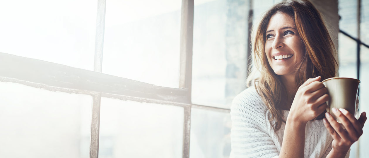 Smiling woman looking out through a sunlit window